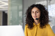 © Liubomir - A woman with curly hair wearing a headset, looking attentively at a computer screen, likely providing customer service or support in a modern office.