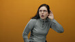 © Krakenimages.com - Woman with glasses displaying various facial expressions against an orange background, wearing a gray sweater, looking confused, listening, and curiously engaged.