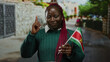 © Krakenimages.com - Woman smiling on city street holding suriname flag with confident gesture, conveying cultural pride and diversity, wearing green sweater outdoors in urban setting.