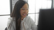 © Krakenimages.com - Asian woman smiling in a modern office setting, wearing glasses, reflecting a professional and cheerful work environment.