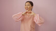 © Krakenimages.com - Woman smiles while forming a heart with her hands against a pink background, displaying charm and positive energy, embodying youth and beauty.