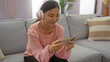 © Krakenimages.com - Woman playing smartphone in relaxed living room setting, wearing headphones and pink blouse, showcasing indoor leisure at home