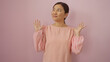 © Krakenimages.com - Woman smiling in pink blouse against a pastel pink background, showcasing joy and charm with hands raised, embodying grace and elegance.