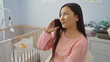 © Krakenimages.com - Woman talking on phone in baby room with cradle, wearing pink blouse, portraying a calm atmosphere at home, captured in modern indoor setting with soft lighting.