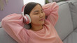 © Krakenimages.com - Woman relaxing on a couch wearing headphones in a cozy apartment, enjoying a peaceful and tranquil moment indoors, with pink attire highlighting her serene expression.