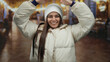 © Krakenimages.com - Hispanic woman in a white jacket makes a roof gesture indoors at a church, smiling warmly under soft lighting, creating a cozy atmosphere.
