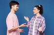 © ViDi Studio - Side view young couple two friends family man woman wear pink casual clothes together look to each other spread hands speak talk isolated on plain blue background studio portrait. Lifestyle concept.