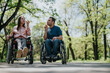 © qunica.com - A couple in wheelchairs spending time outdoors on a sunny day, enjoying blowing bubbles together in a quiet park surrounded by trees.