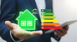 © HARRY - Businessman holding glowing green house icon with energy efficiency ratings A to G, showcasing eco-friendly home concept and sustainable living solutions.