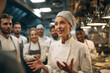 © Katie R - female head chef gesturing while briefing diverse kitchen staff, lively team atmosphere