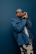 © Bliss - Young man showcases style with denim jacket against a blue backdrop