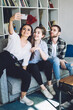 © BullRun - Friends taking selfie while sitting on sofa at home