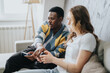© qunica.com - A diverse couple sitting on a comfortable couch, engaging in a video game. The scene captures a warm and interactive atmosphere, emphasizing fun and connection.