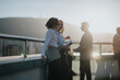 © qunica.com - A multicultural group of colleagues engaged in brainstorming on a high tower balcony. The sunset provides a warm backdrop, highlighting collaboration and teamwork among the diverse business people