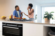 © Wavebreak Media - Talking diverse couple gesturing and eating at kitchen island, with condiment bottles, copy space