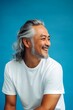 © R - A confident man making a stylish impression. Blue solid background. Idea of style for aging men. Fashionable men's wavy fringe haircut - midlife asian man with long hair.