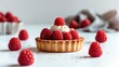© Sona - Fresh raspberry tart with cream and raspberries on top, surrounded by scattered raspberries on a white surface.