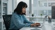 © Lato - Young woman coding on a laptop in a modern office with large windows and greenery in the background