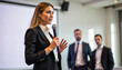 © Mathias Rosenthal - A woman in a business suit speaking into a microphone at a conference with two men in the background. - Generic AI Image