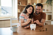 © Migma_Agency - Happy couple saving money together at home putting coins in piggy bank