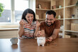 © Migma_Agency - Happy couple saving money at home putting coins in piggy bank