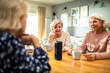 © Marko Geber - Senior women talking around table with smart speaker and coffee cups