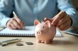 © Vadym - Person puts coin piggy bank. Concept finance, savings, investment, wealth. Piggy bank, coin, pen, notepad on table. Planning finances, retirement, banking.