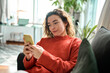 © insta_photos - Relaxed young woman sitting on couch using cell phone technology, happy lady holding smartphone, scrolling, looking at cellphone enjoying doing online ecommerce shopping chatting in mobile ai apps.