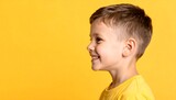 A young boy smiles broadly, his profile highlighted against a vibrant yellow background.