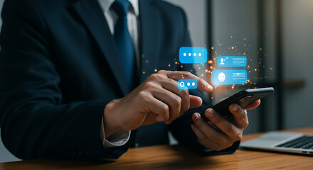 Man in suit interacting with chat bubbles on a smartphone at a desk with a laptop nearby