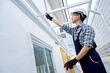 © Summer Paradive - Asian male foreman or construction worker climbing up on an aluminium ladder pointing at the roof structure of a new house. Professional builder working at housing project building site