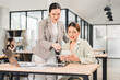 © PRIME STOCK LAB - Two businesswomen collaborating on digital tablet in modern office, showing teamwork and positive communication with laptops and documents on desk