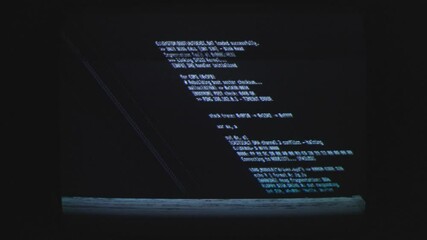Coding text script in display against a black background at computer monitor.