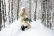 © Светлана Высокос - A beautiful woman with short blonde hair is dressed in a white fur coat and black boots. She stands against the background of a snowy landscape with a basket and a bouquet of fir branches.