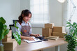 © snowing12 - Asian Young Woman Calculating Business Expenses for Online Shop Order with Boxes and Clipboard to Prepare Delivery to Customer E Commerce from Home Office