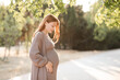 © morrowlight - Smiling pregnant woman 24-29 year old holding tummy wearing knitted clothes over nature in park outdoors. Maternity.