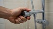 © Lucas - Close-up of a male hand turning off a shower, focus on fingers and water control, modern bathroom setting, concept of water conservation, clean and minimalistic environment, soft natural lighting.