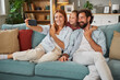 © Stockphotodirectors - A family of three smiles happily as they take a selfie on a comfortable sofa in their well-decorated living room, capturing a joyful moment of togetherness.