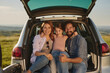 © Stockphotodirectors - A cheerful family is gathered around the open trunk of their car, smiling and enjoying quality time together in a beautiful outdoor area during the afternoon.