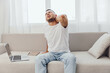 © SHOTPRIME STUDIO - Painful man stretching his neck while sitting on a modern couch. The image captures discomfort, home office environment, and casual attire for a relatable vibe.