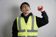 © yashis007 - Energetic young Asian man in a safety vest and gloves, shouting and raising his fist in a gesture of triumph, protest, or excitement.