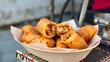© the last of art - Deep-fried spring rolls cut in half, showing filling, served in a paper basket on a weathered street cart – evening light