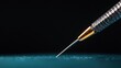 © GATE 22 - Close-up of a needle with a gold-colored tip. the needle is resting on a blue surface with a black background.