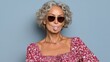 © Nataliia_Trushchenko - Mature woman with curly gray hair wearing sunglasses and a floral dress, blowing a bubble with chewing gum, exuding confidence and playfulness against a soft blue background, showcasing a fun and vibr