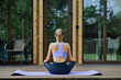 © boomeart - Back view of a woman sits on a yoga mat placed on a wooden terrace of tiny house