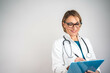 © Nenad - Confident mature female doctor writing on clipboard, isolated background