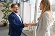 © Moon Safari - Smiling businessman in eyeglasses shaking hands with female partner after a successful business deal in meeting room
