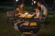 © VStudio - A family is having a barbecue in the backyard. There are four people, including a man and a woman, and a child. They are sitting around a table with food, including hot dogs and hamburgers