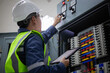 © JD Studio - Engineer in safety vest and helmet performs inspection on electrical load center unit adjusting controls while holding tablet to ensure proper function and safety compliance