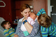 © Irina Schmidt - Mother holding newborn baby girl in hospital bed, with two sons sitting beside her. Real life, real people moment of family love, siblings bonding, and joy of welcoming a new child.